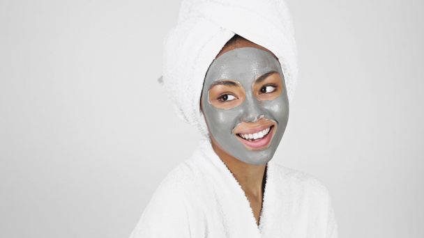 Ευτυχισμένη Αφροαμερικανή γυναίκα με πετσέτα στο κεφάλι και γκρι μάσκα προσώπου απομονωμένη σε γκρι  - Φωτογραφία, εικόνα