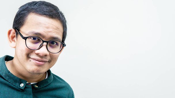Portrait of an Asian Malay man with green casual shirt and spectacles smiling and looking at the camera with copy space on isolated white background. - Photo, Image
