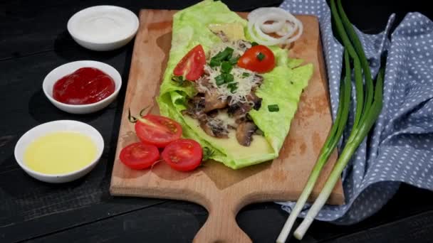 Vegetarian green pita bread with mushrooms and cheese rotates on a wooden table. Around the tomatoes, greens and various sauces - Footage, Video