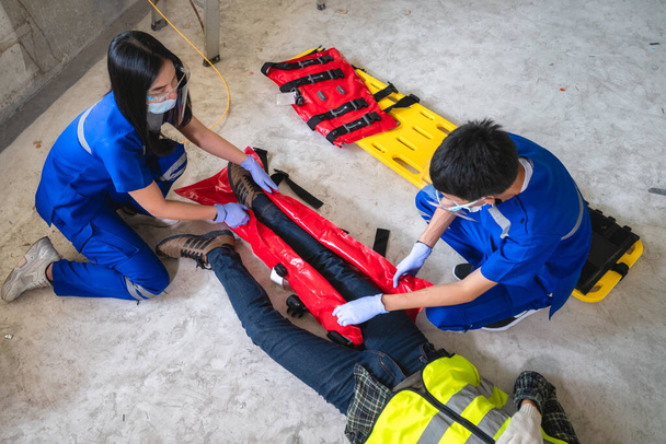 Ιατρικές ομάδες έκτακτης ανάγκης βοηθούν έναν εργάτη με ένα σπασμένο πόδι σε ένα εργοτάξιο. Ομάδα ασφαλείας βοήθεια εργατικό ατύχημα. - Φωτογραφία, εικόνα
