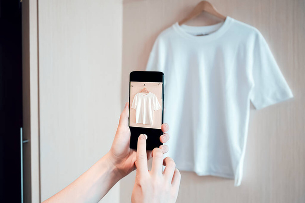 Nainen ottaa valokuvan älypuhelimella käytettyjen vaatteiden jälleenmyyntiin tai hyväntekeväisyyteen - Valokuva, kuva