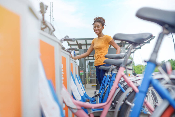 自転車シェアリングシティサービスで自転車を借りる若いアフロ女性 - 写真・画像