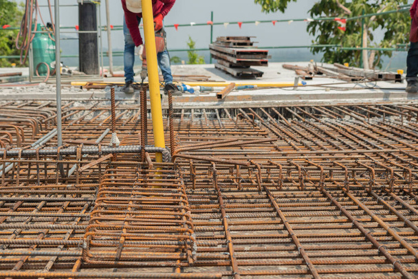 Steel bars on concrete floor for pouring concrete have red rust and a background workers are removing concrete, working at heights and mountain construction. - Photo, Image