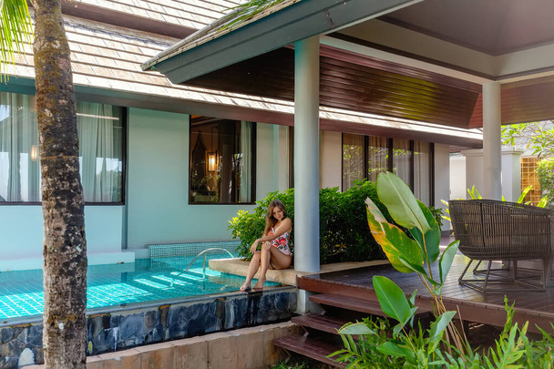 Young Woman in Swimwear Sitting near Swimming Pool on Tropical Luxury Villa - Фото, зображення