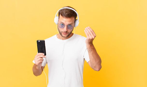 making capice or money gesture, telling you to pay, listening music with headphones and a smartphone - 写真・画像