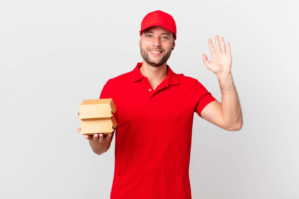 burger deliver man smiling happily, waving hand, welcoming and greeting you - Фото, изображение