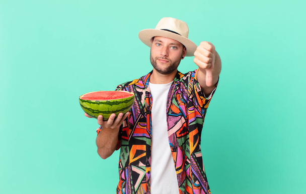 handsome traveler man feeling cross,showing thumbs down and holding a watermelon. holidays concept - Foto, imagen