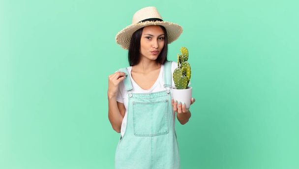 pretty farmer woman looking arrogant, successful, positive and proud and holding a cactus - Foto, Bild