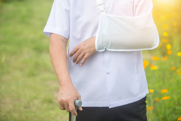 old man holding a cane broken arm after accident with wear arm splint in the park - Fotografie, Obrázek