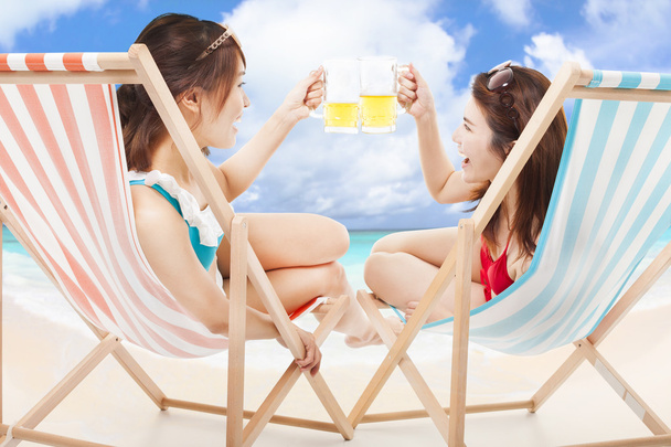 two sunshine girl holding beer cheers  on a beach chair - Fotografie, Obrázek