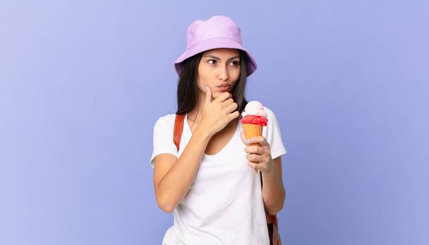 pretty hispanic tourist thinking, feeling doubtful and confused and holding an ice cream - Foto, afbeelding