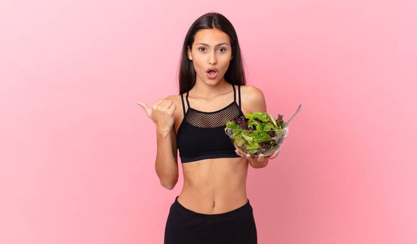 hispanic fitness woman looking astonished in disbelief and holding a salad - Фото, изображение
