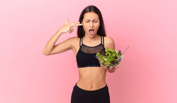 hispanic fitness woman looking unhappy and stressed, suicide gesture making gun sign and holding a salad - Photo, Image