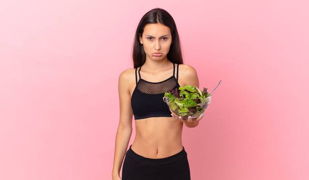 hispanic fitness woman feeling sad and whiney with an unhappy look and crying and holding a salad - Fotó, kép