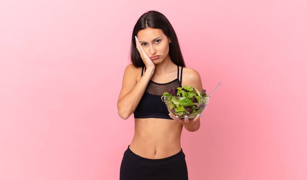 hispanic fitness woman feeling bored, frustrated and sleepy after a tiresome and holding a salad - Fotó, kép