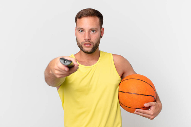 handsome man with a basketball ball and choosing a channel with a controller - 写真・画像