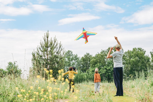 Dad and sons let a kite in the street. Happy childhood with dad. Active games on the street. A kite is high in the sky. - Фото, изображение