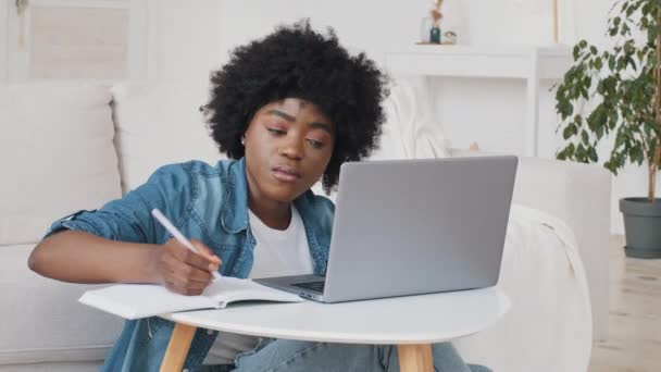 Зосереджена афроамериканська студентка за допомогою ноутбука для навчання або серфінгу соціальних медіа сидить на дивані вдома, чорна тисячолітня дівчинка навчається онлайн на комп'ютерних нотатках або виправленнях роблять документи - Кадри, відео
