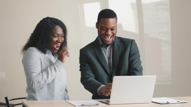 Joven mentor masculino africano muy alegre y pasante femenina de raza mixta mirando la pantalla de la computadora portátil, emocionada por las increíbles buenas noticias. Felices compañeros de trabajo celebrando recepción atrajo notificación de inversión - Imágenes, Vídeo