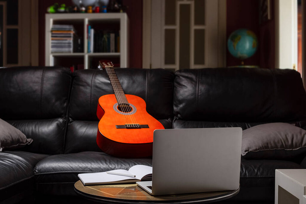 Κιθάρας στον καναπέ στο σπίτι έτοιμη να λάβει μαθήματα κιθάρας σε απευθείας σύνδεση. - Φωτογραφία, εικόνα