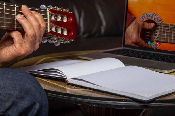 Izolowany obraz dłoni człowieka grającego na gitarze akustycznej i oglądającego kurs online na laptopie podczas treningu w domu. - Zdjęcie, obraz