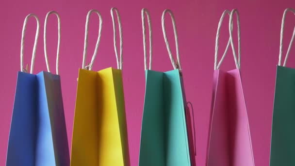 Fila de coloridas bolsas de regalo sobre fondo rosa plano medio - Imágenes, Vídeo