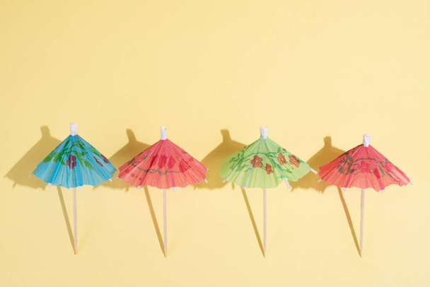 Summer party background, multicolored cocktail umbrellas on yellow background in bright sunlight, close up. - Foto, Imagen