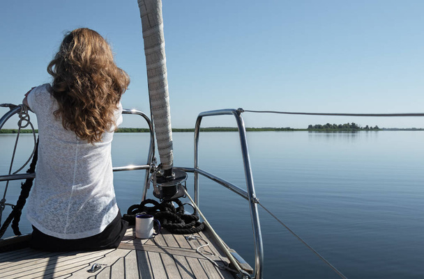 lány fehér póló és hosszú göndör haj néz felülete víz a fedélzeten a jacht. Nyári hétvége a vízen - Fotó, kép