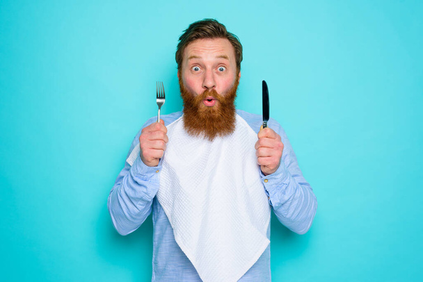 Shocked man with tattoos is ready to eat something with cutlery in hand - Photo, Image