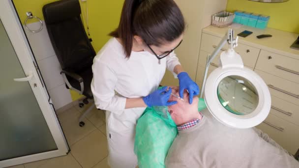 Молодая женщина в перчатках делает красоту анти-возрастной инъекции для пожилых мужчин во время лечения биоревитализации - Кадры, видео