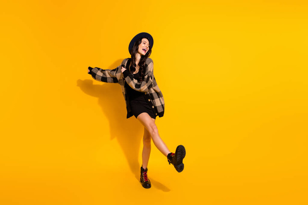 Photo of funny excited young lady dance wear black hat checkered coat isolated yellow color background - Foto, afbeelding