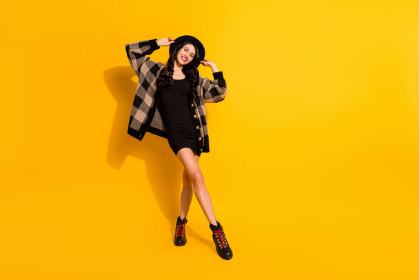 Full length photo of stunning happy positive young lady wear plaid coat mini black dress hat isolated on yellow color background - Foto, afbeelding
