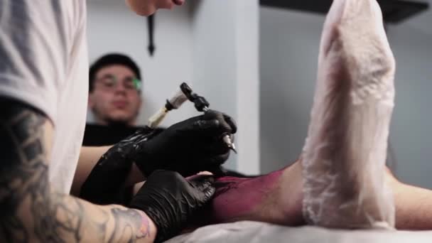 Tetovací salon - klient leží na gauči a nechává si udělat tetování na noze - Záběry, video
