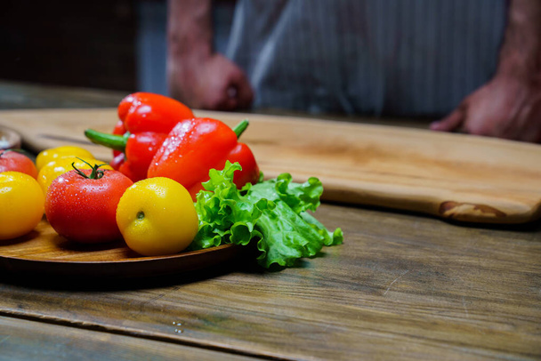 yellow and red tomatoes, lettuce and bell pepper with water drops. man in apron. - Foto, afbeelding