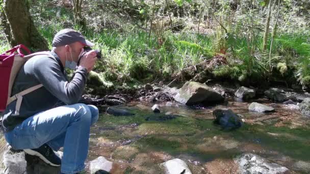 El hombre de gorra se agachó tomando fotos con máscara en un río. Personas en la naturaleza. - Metraje, vídeo