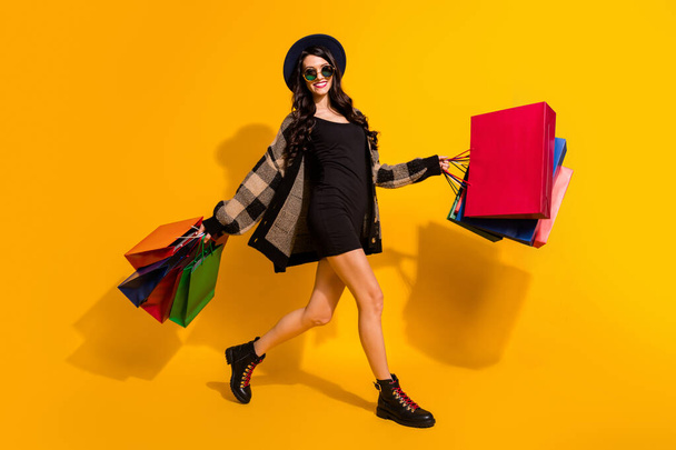 Foto de shopaholic lady hold paquetes caminar desgaste retro especificaciones sombrero a cuadros chaqueta botas aislado color amarillo fondo - Foto, imagen