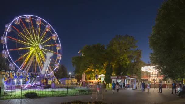 Forog a megvilágított vonzerő óriáskerék és fényes körhinta körhinta nyári esténként a városi vidámparkban - Felvétel, videó