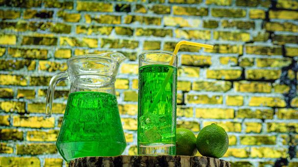 Fruit green drink in a glass against a brick wall background, green lemonade in a glass with lime. Summer drink with ice - Zdjęcie, obraz