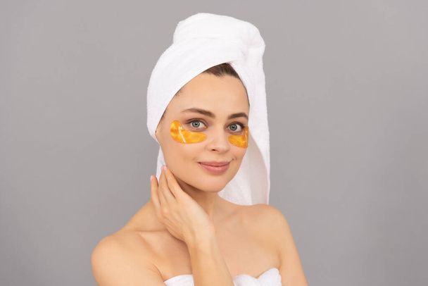 テリータオルの若い女性は肌、スキンケアのための顔の黄金の目のパッチを使用 - 写真・画像