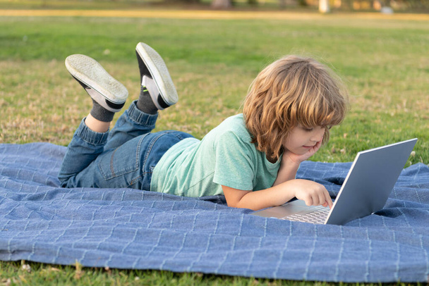 petit enfant utiliser un ordinateur portable sans fil moderne sur l'herbe du parc, étudier en ligne - Photo, image