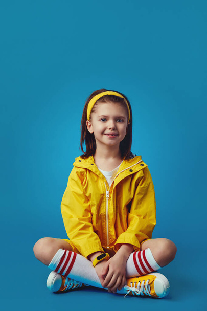 Meisje in felgele outfit, glimlachend naar de camera tijdens het zitten gekruiste benen - Foto, afbeelding