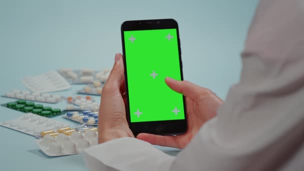 Nahaufnahme, Arzt-Handbewegungen auf dem Smartphone, grüner Bildschirm und medizinische Pillen-Blisterverpackungen auf blauem Hintergrund. - Filmmaterial, Video