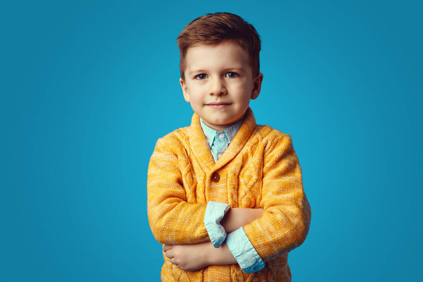 intelligente piccolo nerd ragazzo in piedi con le braccia incrociate su sfondo blu - Foto, immagini