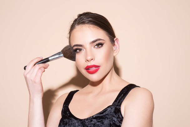 Beautiful young woman with clean fresh skin holding makeup brush. Applying tone to skin. - Foto, imagen