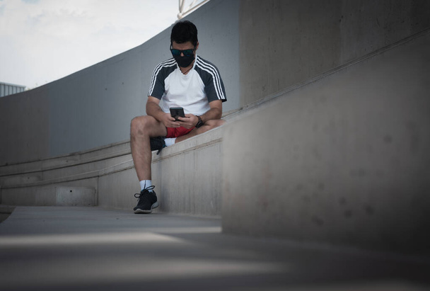 Mann in Sportkleidung blickt auf der Tribüne auf sein Smartphone - Foto, Bild