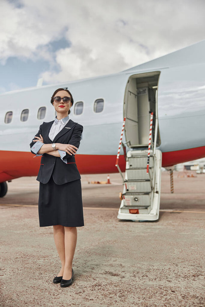 Selbstbewusste Stewardess auf Landebahn in der Nähe von Flugzeug-Jet - Foto, Bild