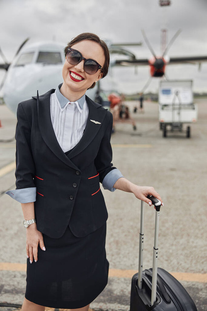 Stewardess mit Gepäck auf Landebahn nahe Flugzeug - Foto, Bild