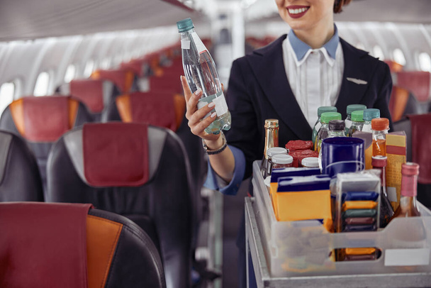 Стюардеса тримає пляшку води в салоні літака
 - Фото, зображення