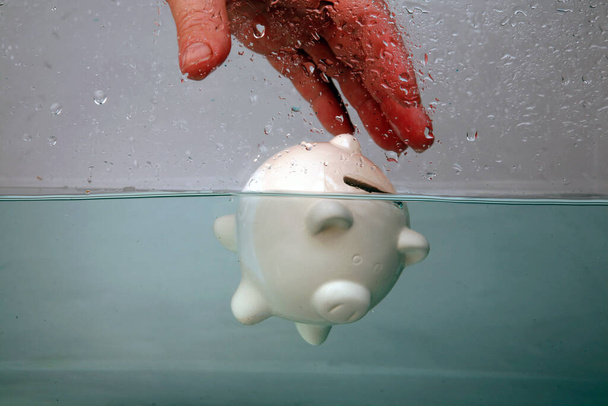 Drowning in Debt. a piggy bank sinks in dark murky water. drowning in debt. keeping your head above water. financial concepts. help at financial crisis. Financial Aid and rescue from debt problems. drowning piggy bank sinking in blue water.  - Fotoğraf, Görsel