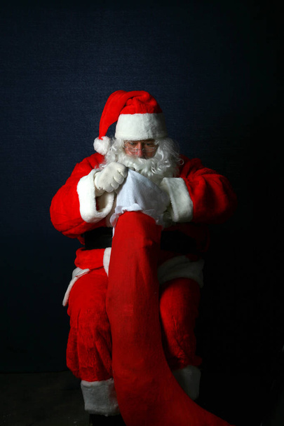 Meia-noite de Natal. Papai Noel enche uma meia de Natal com presentes e guloseimas. Feliz Natal. Boas festas..  - Foto, Imagem